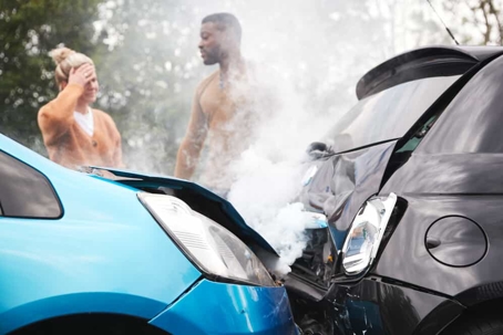 Woman covers her head in grief while standing next to a man and looking at their damaged vehicles that collided