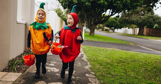 two young kids walking on a sidewalk wearing pumpkin halloween costumes