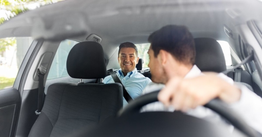 two men in a small car - one in the backseat and the driver turning to look at the passenger