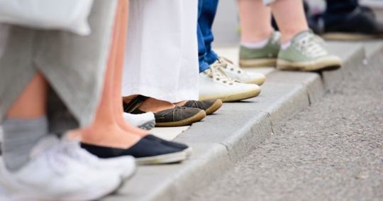 Feet of pedestrians who are waiting to cross the road