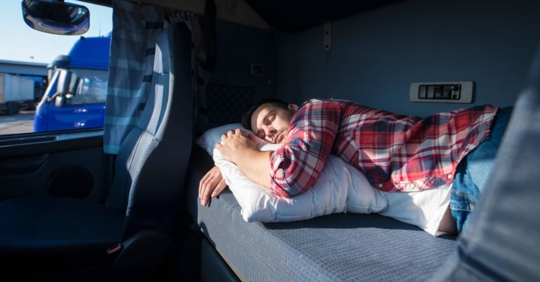 truck driver lying in the sleeper berth holding a pillow